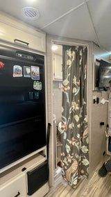 RV rental interior features a black refrigerator with magnets, a bathroom entry with floral curtain, and a wall-mounted TV.