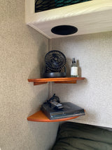 Corner of an RV rental: built-in shelves with a fan, room spray, and DVD player. Speaker overhead for entertainment.