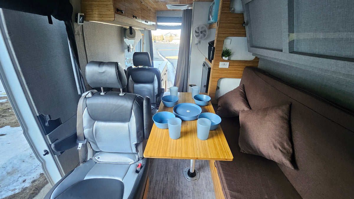 This RV rental interior features a bamboo dining table set with dishes, swiveling seats, and cozy couch.