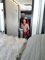 Happy man inside a comfy RV rental, showcasing the cozy living area with storage and a fluffy blanket.