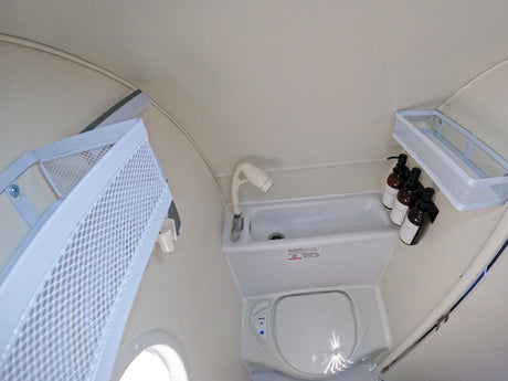 Compact RV rental bathroom: features a toilet, sink with shower sprayer, and wall-mounted baskets for soap and shampoo.
