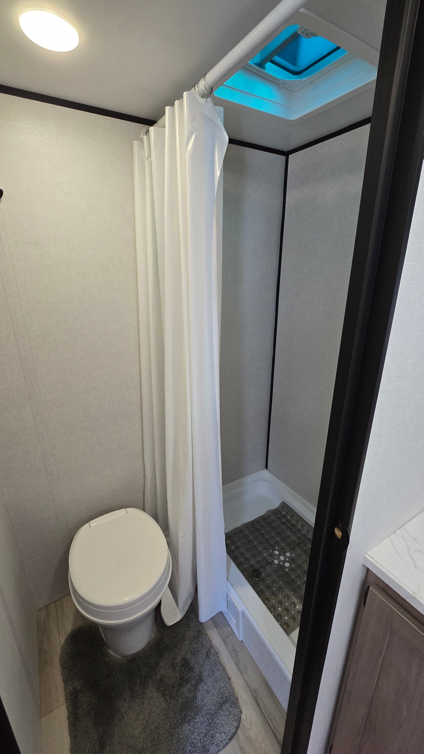 Compact rv rental bathroom with white toilet, shower, ceiling light, and sky vent. Clean and functional space.