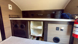 View of an RV rental's bed area, featuring integrated storage, a stereo, climate control, and a fire extinguisher for safety.