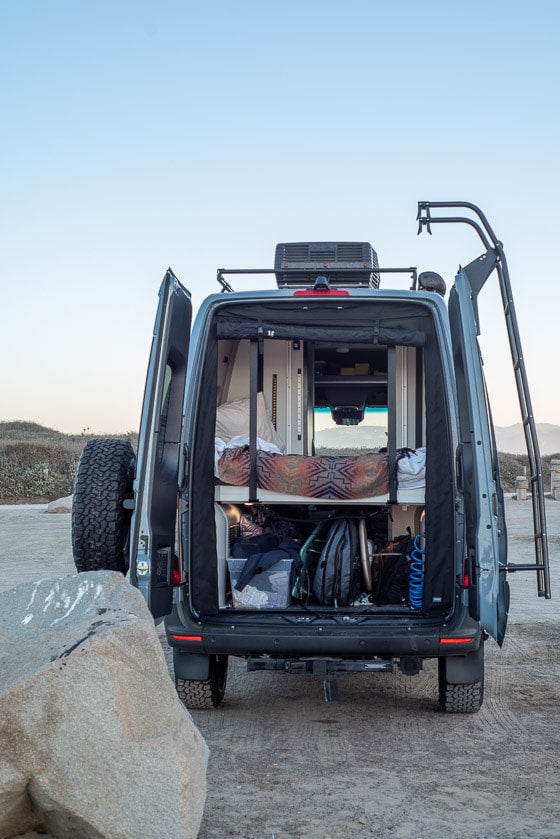 Open back of an RV rental camper van showing bed, gear storage, and rooftop AC unit. Equipped for adventure travel. — photo 4