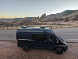 Black camper van parked by scenic red rock formations at dusk, a perfect RV rental for outdoor adventures.