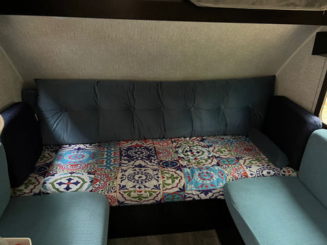 Cozy RV rental interior featuring a blue tufted sofa bed and colorful patterned bedding, with light blue seating in the foreground.