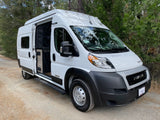 White Winnebago camper van rv rental parked on a dirt road, side door open. Perfect for forest adventures.