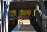 Inside a custom rv rental van: bed, front seats, and a serene nature view through the windows.