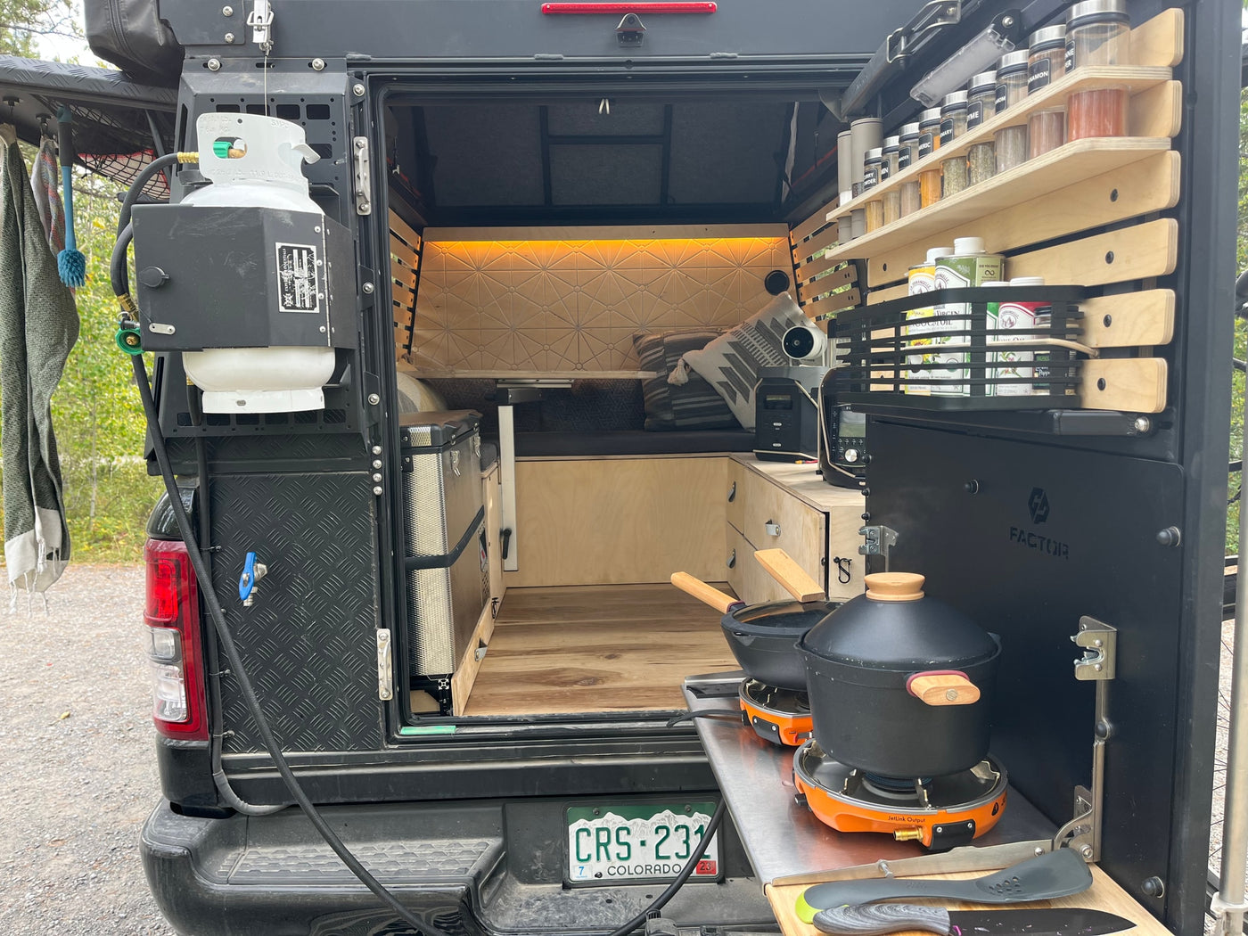 Rear view of a custom camper, ideal for an **rv rental** adventure. Features an outdoor kitchen with propane, a spice rack, and a cozy interior with a bed and storage. — photo 15