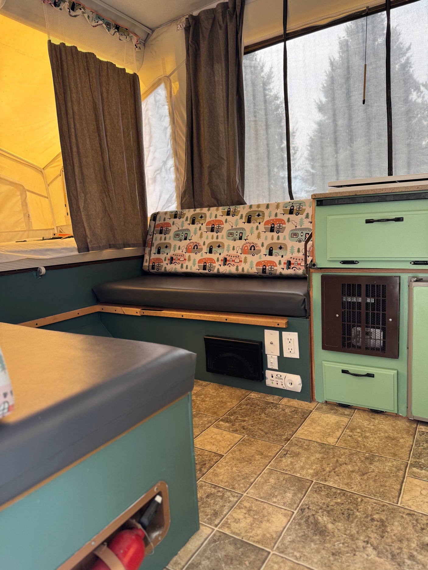 Cozy RV rental interior with patterned camper cushions, green cabinets, and window views of trees outside.
