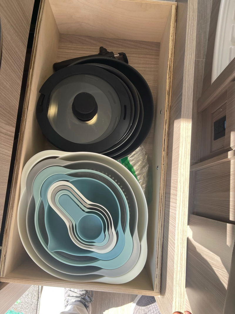 RV rental kitchen drawer neatly organized with nesting pots & lids, plus a stack of colorful nesting bowls and measuring cups. — photo 17