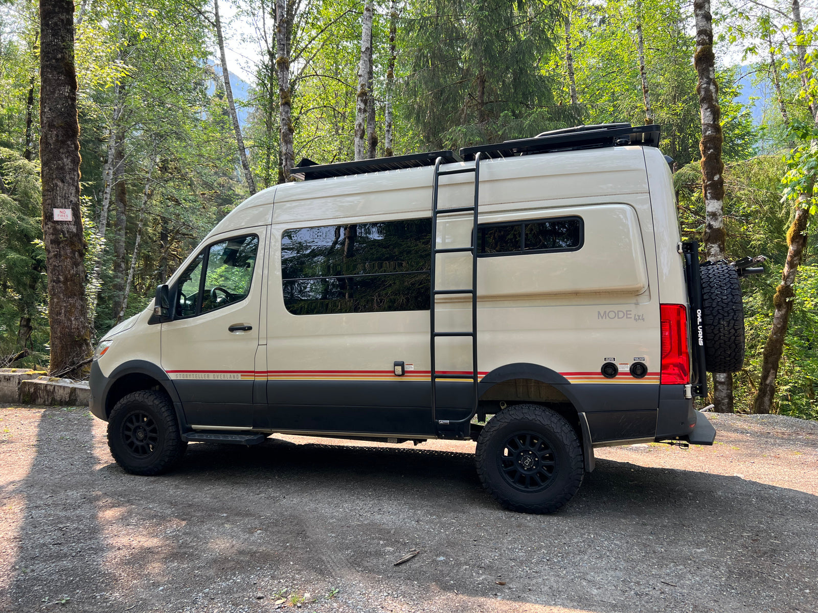 Cream-colored camper van equipped for overland adventures, parked on gravel in a sunny forest. Ideal for rv rental trips.