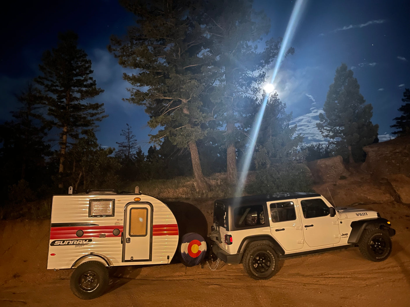 White Jeep and SunRay Sport teardrop RV rental parked under a bright moon at night for camping adventure.
