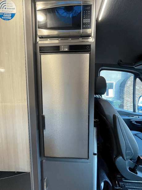 Compact kitchen in an RV rental featuring a built-in stainless steel microwave above a tall refrigerator.