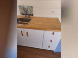 Compact RV kitchen with sink, wood counter, white cabinets & floral backsplash, perfect for your RV rental adventure.
