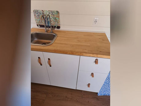 Compact RV kitchen with sink, wood counter, white cabinets & floral backsplash, perfect for your RV rental adventure.