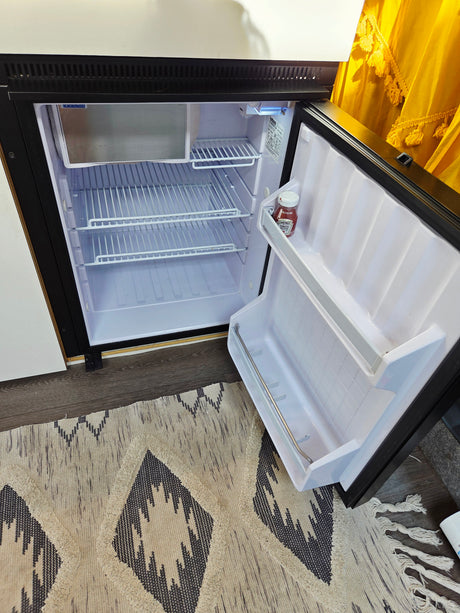 Inside a clean, open compact refrigerator in an rv rental, featuring white wire shelves and a single ketchup bottle.