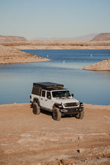 White Jeep Gladiator with rooftop tent by a lake. Perfect RV rental for off-road overlanding adventures in the desert.