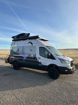 This custom RV rental, a gray adventure van, features a vivid outdoor sports wrap & rooftop kayak.