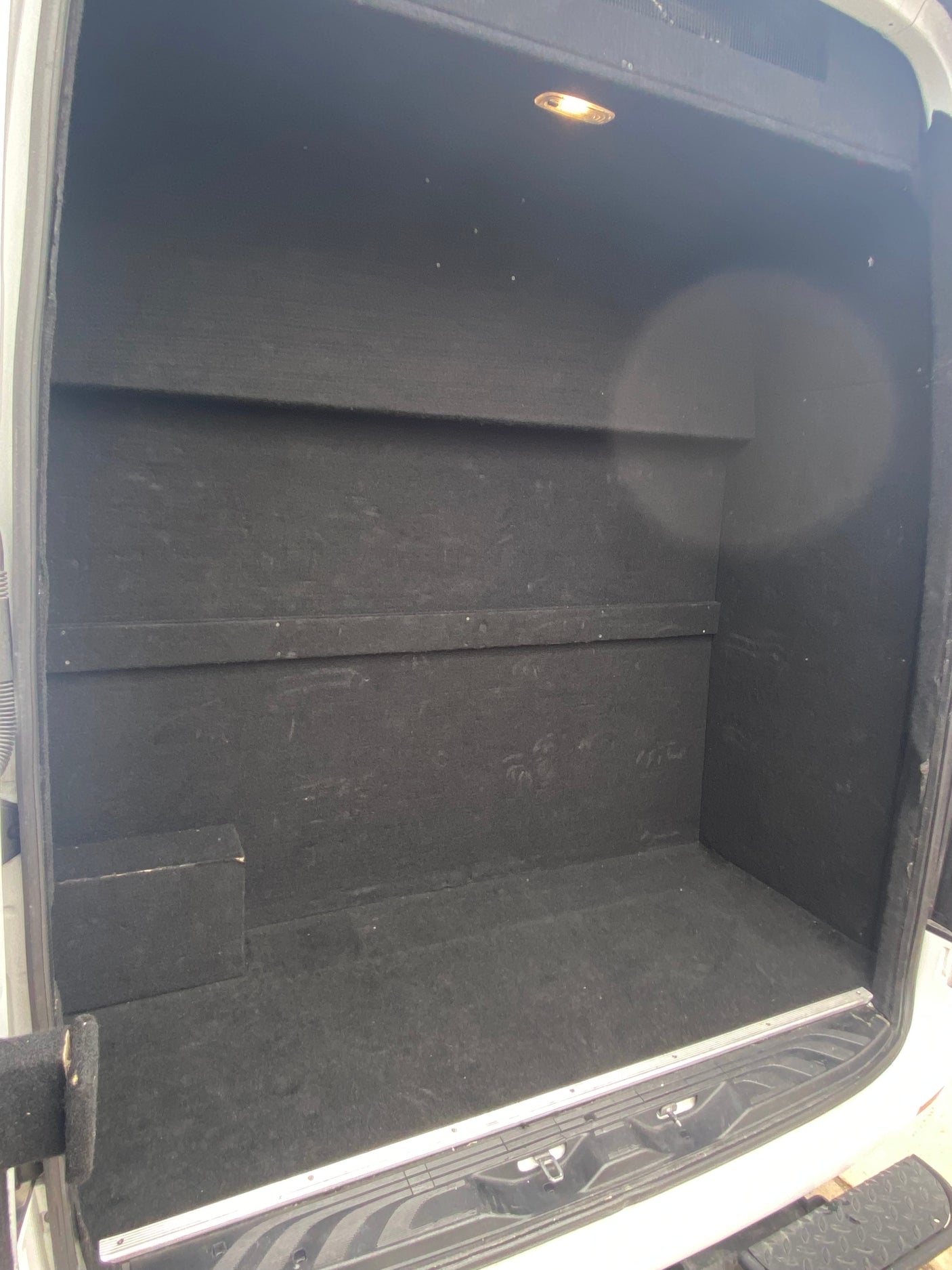 Inside a custom-built RV rental cargo van, featuring a black-lined storage area with built-in shelves and an overhead light.