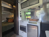 This modern rv rental features a cozy bedroom and a well-equipped kitchen with a microwave, fridge, and sink.