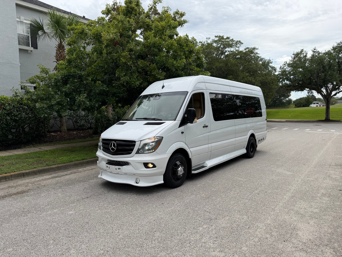 White Mercedes Sprinter conversion van, suitable for rv rental, parked on an overcast day with green trees and a building.
