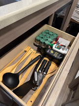 This RV rental kitchen drawer holds cooking utensils, spices, olive oil, and insect repellent, neatly organized for travel.