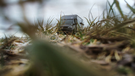 A dark Mercedes-Benz Sprinter camper van, seen at a low angle through tall grass. Ideal for an RV rental adventure.