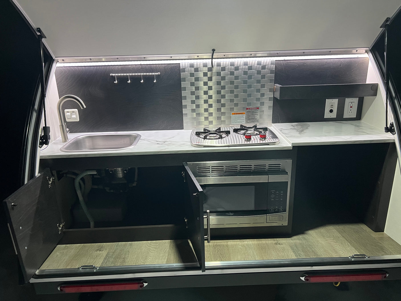 RV rental's outdoor galley: sink, two-burner stove, microwave, and outlets, perfect for convenient campsite cooking.