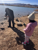 An adult holding a freshly caught fish, with a child and fishing rods by a scenic mountain lake. Perfect RV rental outdoor adventure.