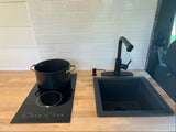 Modern RV rental kitchen with black induction cooktop, pot, black sink, and gooseneck faucet on a wood counter.