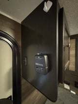 RV rental: Suburban thermostat on a dark panel with light switch and storage cabinet, featuring a white wall hook above.