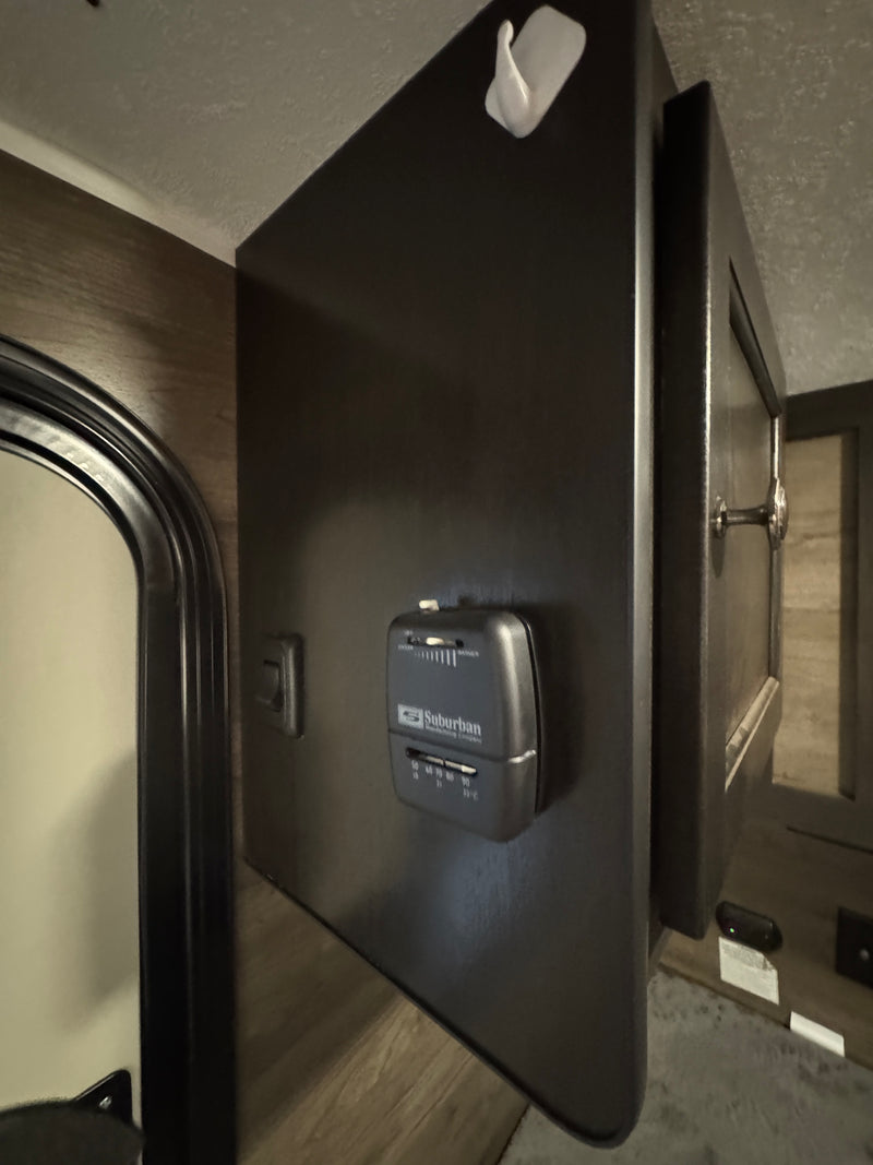 RV rental: Suburban thermostat on a dark panel with light switch and storage cabinet, featuring a white wall hook above. — photo 7