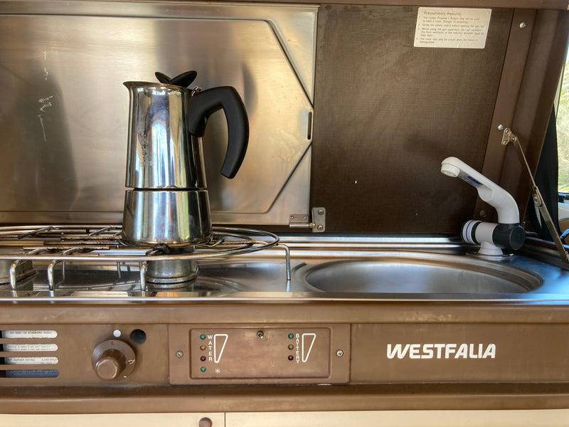 An RV rental's compact Westfalia kitchen with a Moka pot on the stove, sink, and water/battery level indicators. — photo 6