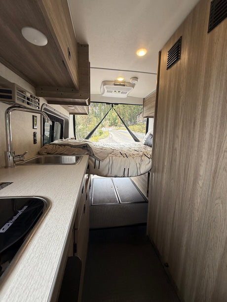 RV rental interior: cozy camper van with kitchenette, raised bed, & scenic view for road trips.