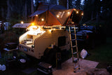  complete with a rooftop tent for off-road adventures.|Muddy motocross track winds through dense trees. An RV rental-style trailer setup and vans are parked trackside for the event.|Illuminated RV rental teardrop trailer with a cozy iKamper rooftop tent & outdoor kitchen
