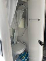 Compact RV rental bathroom featuring a shower, toilet, and a towel bar on the right wall.