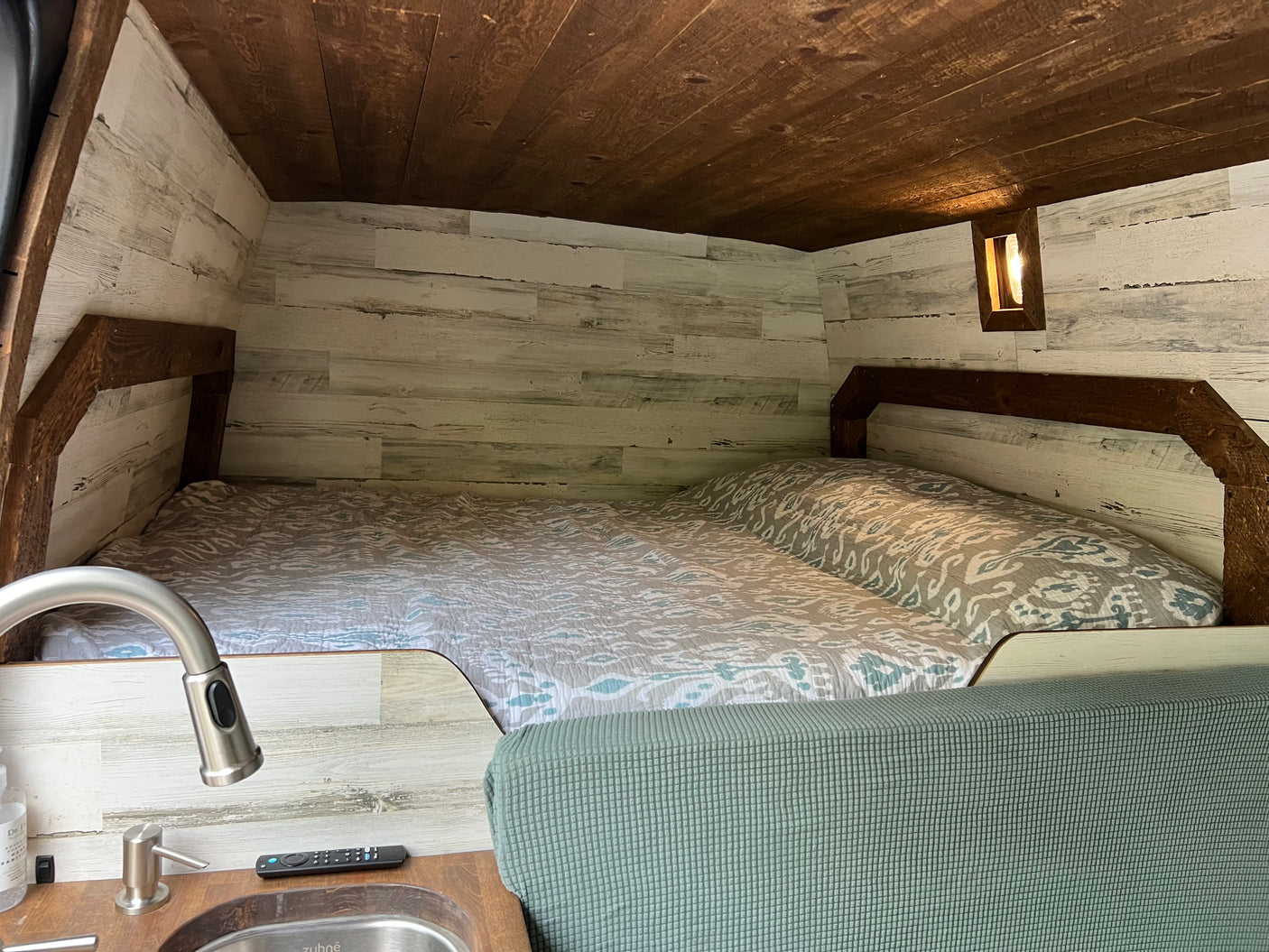 Step inside this cozy rv rental featuring a comfortable bed, stylish wood paneling, and a compact sink area.