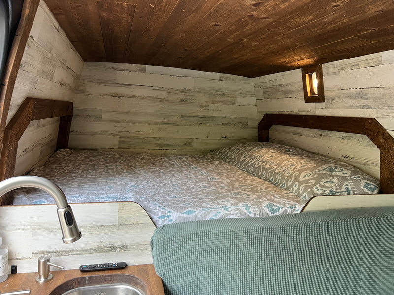 Step inside this cozy rv rental featuring a comfortable bed, stylish wood paneling, and a compact sink area. — photo 10