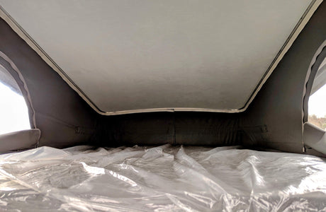 Pop-top rv rental bed interior: a mattress with crinkled clear plastic, light ceiling, and dark fabric walls.