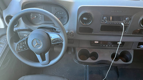RV rental interior: Mercedes-Benz Sprinter dashboard, steering wheel, instrument cluster, radio, and cupholders.