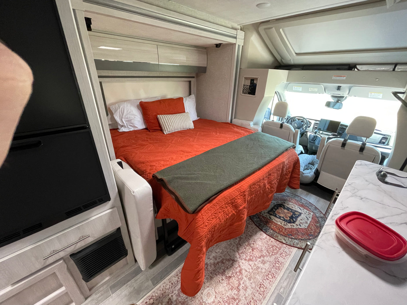 Inside a modern RV rental, featuring a comfortable bed, integrated kitchen, and forward cockpit.