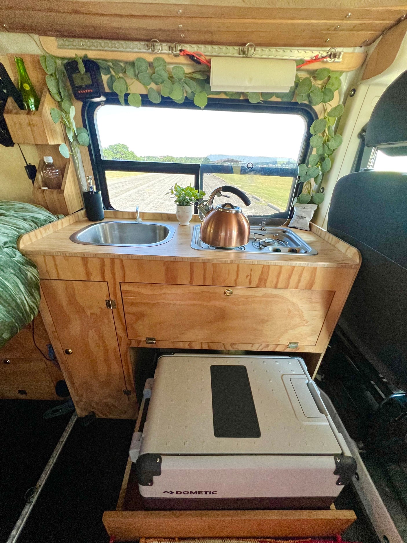 Cozy rv rental kitchen with sink, stove, Dometic fridge, and scenic window view, perfect for van life adventures.