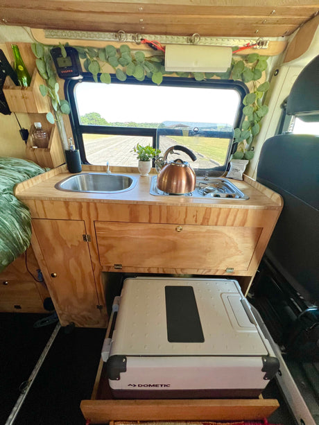 Cozy rv rental kitchen with sink, stove, Dometic fridge, and scenic window view, perfect for van life adventures.