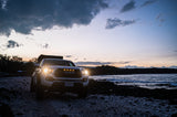 White Tacoma with rooftop tent on a rocky beach at dusk. Perfect coastal camping. Book your RV rental adventure!