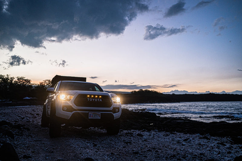 White Tacoma with rooftop tent on a rocky beach at dusk. Perfect coastal camping. Book your RV rental adventure! — photo 12