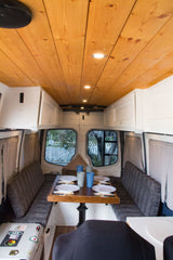 Inside an RV rental: a warm wooden ceiling, bright lights, a dining table set for four, and cozy bench seating.