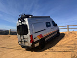 Silver Sprinter camper van with retro stripes on a dirt hilltop overlooking a valley. Perfect rv rental for adventure!