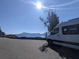 White RV rental van at a sunny mountain lake overlook. Stunning views for a road trip adventure.