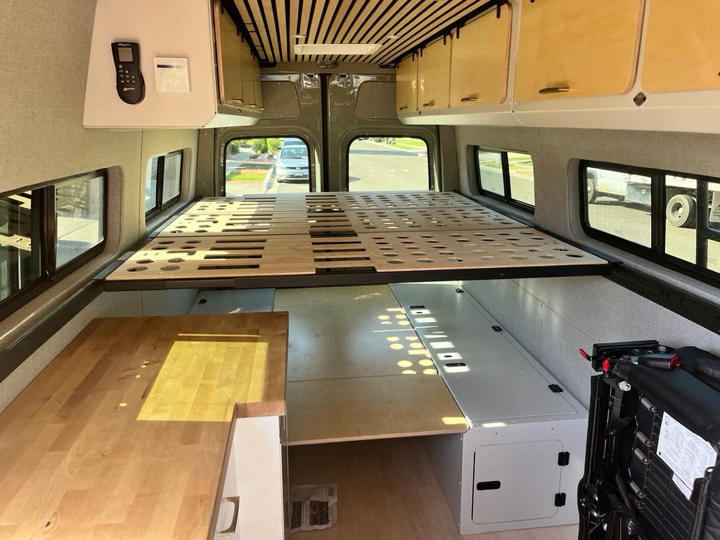 RV rental interior showcasing a multi-piece wooden bed frame, under-bed storage units, and a light wood countertop.